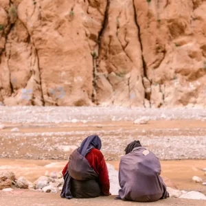 Two local women sitting by the river in the dramatic landscape of Todra Gorge, Morocco