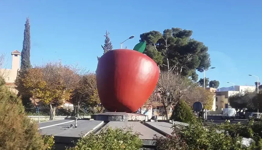 Giant apple sculpture in Midelt, Morocco, symbolizing the region's apple production. The image captures the sculpture in a landscaped area with trees and a clear blue sky.