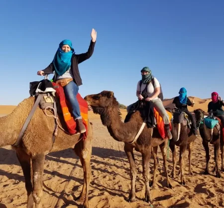 Tourists riding camels in the Moroccan desert, wearing colorful scarves and enjoying the desert scenery.