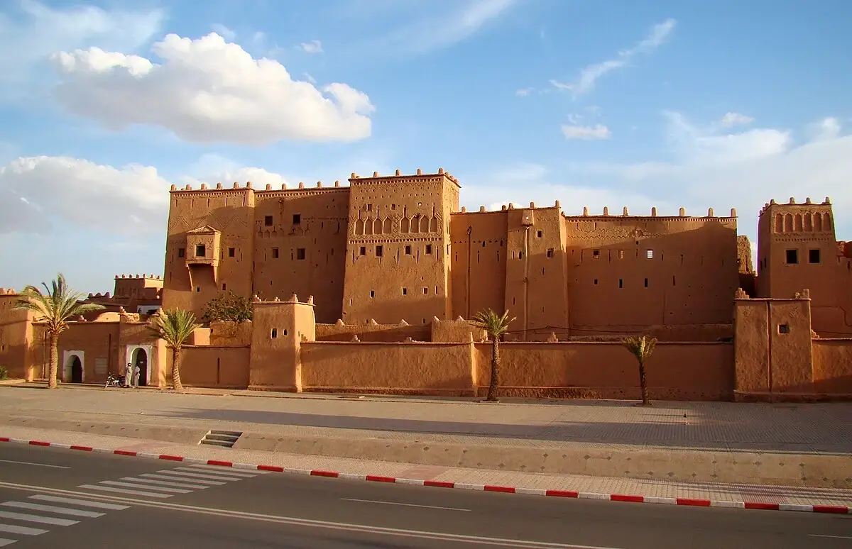 A large, historic kasbah with high walls and fortified towers in Ouarzazate, Morocco, under a clear sky. Keywords: Kasbah Taourirt, Ouarzazate, Morocco, historic, fortress.