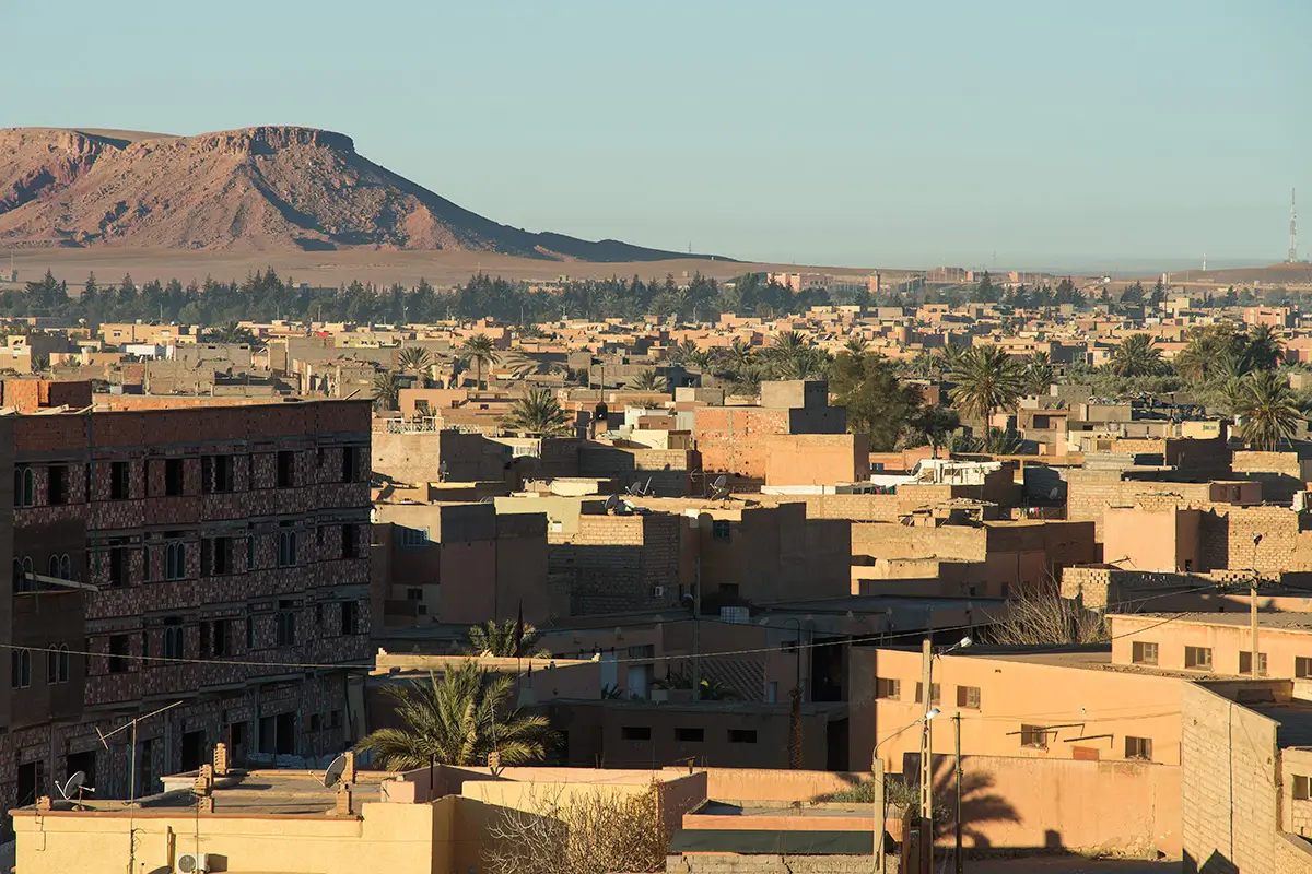 A panoramic view of Errachidia, Morocco, showcasing the city's buildings with a backdrop of a rugged mountain landscape under a clear sky.