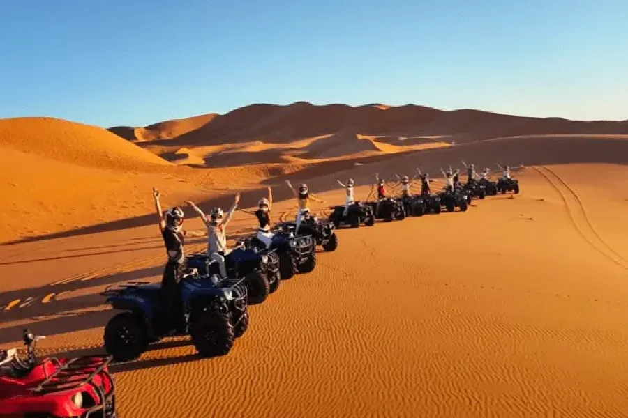 A group of people riding quad bikes in a single file across a vast, sandy desert with rolling dunes in the background. with 6 days from errachidia