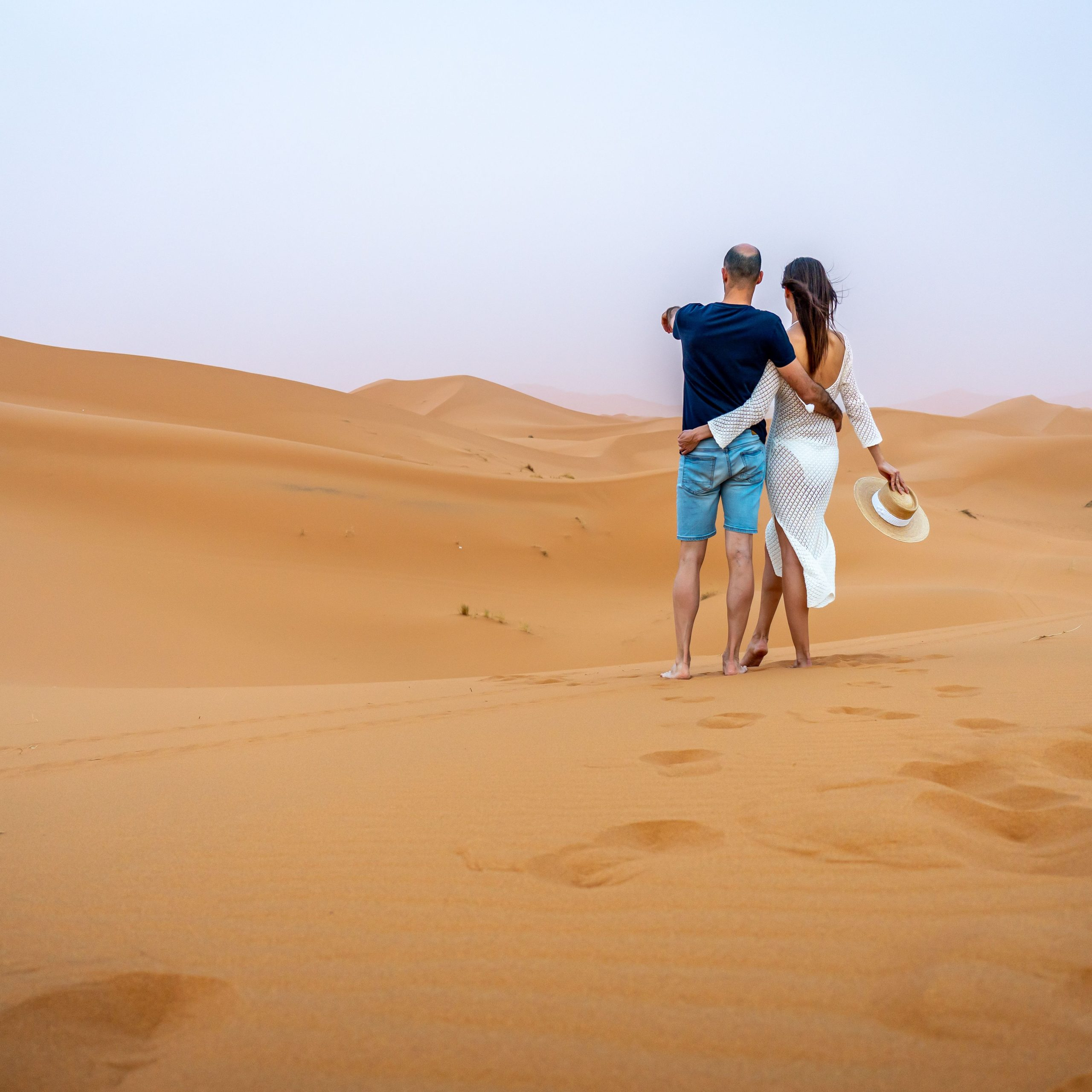 A couple standing on sand dunes in a desert, enjoying the scenic view under a clear sky.