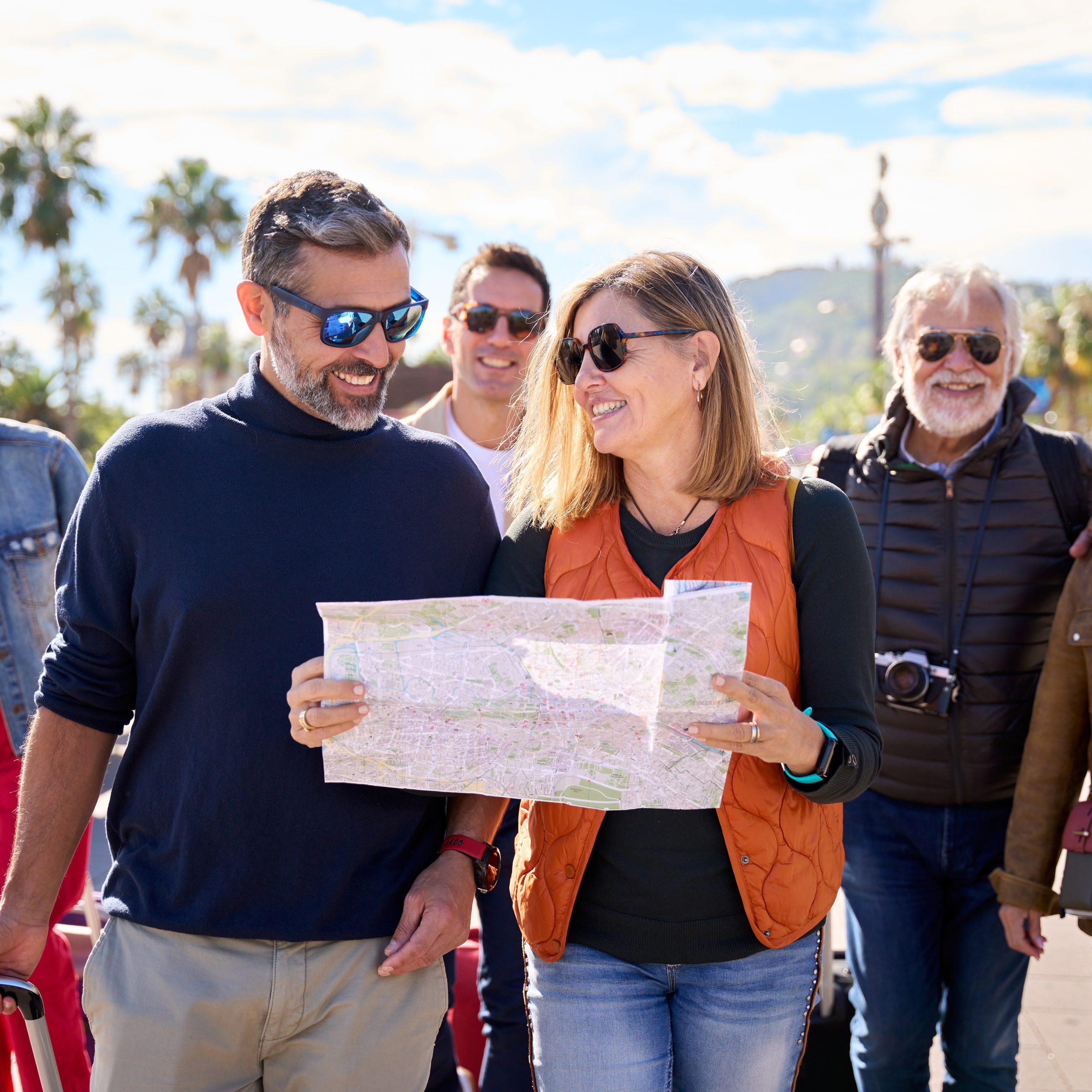 Couple of middle-aged walking and looking and holding a travel map with a group diverse tourist friends with luggage. Tourism of people enjoying their holidays on a European city street